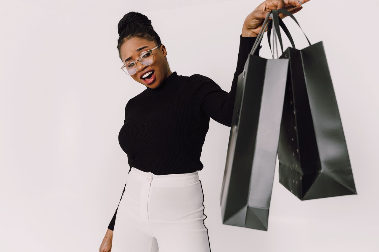 Smiling woman with eyeglasses joyfully holding shopping bags against a white background.